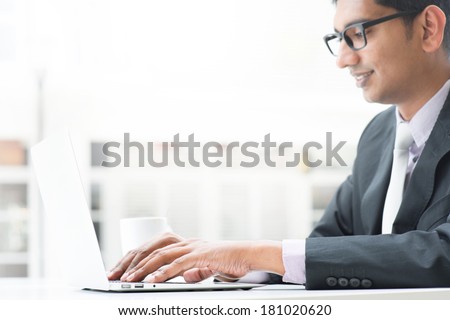 Young Asian Indian businessman using a  laptop  or notebook computer during office break at cafe, relaxing with a cup of coffee. India male business man, real modern office building as background.