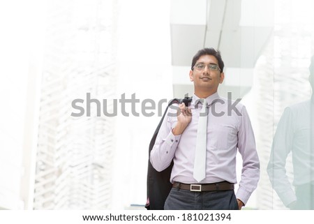 Candid portrait of 30s Asian Indian businessman walking outside office. India male business man, real modern office building as background with natural sunlight.