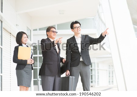 Asian business team meeting, pointing over and having discussion. Modern office background.