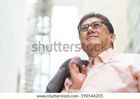 Portrait of 60s Asian Chinese CEO boss smiling and looking away. Senior male businessman, real modern office building as background.