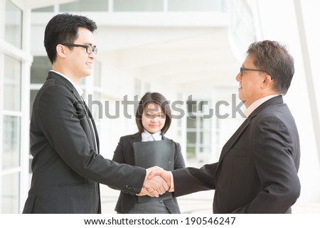 Business deal, Asian businessmen handshaking. Senior CEO hand shake with young executive. Modern  office building architecture background.