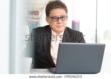 Asian Chinese CEO boss using internet with laptop at cafe. Senior male businessman.