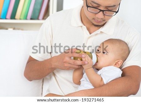 Father bottle feeding baby fruits puree. Asian family lifestyle at home.