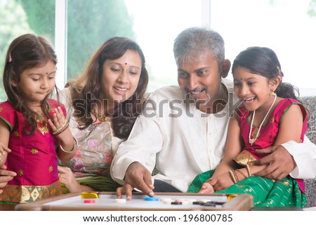 Happy Asian Indian family playing carrom game at home. Parents and children indoor lifestyle.