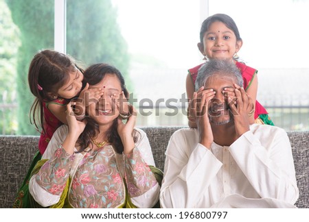Indian family living lifestyle at home. Cute girls in traditional sari costume covering father and mother eyes. Asian parents and children.