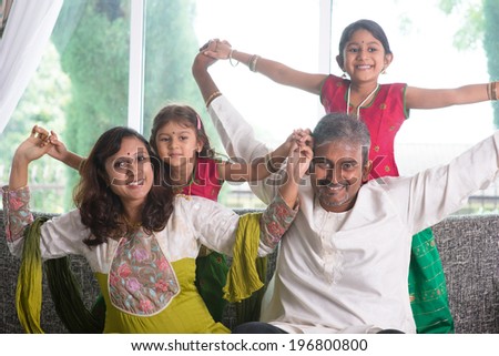 Happy Indian family at home. Asian parents playing with their kids, sitting on sofa. Parents and children indoor lifestyle.