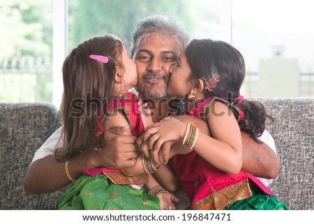 Happy Indian family at home. Two cute Asian girls kissing father, sitting on sofa. Parent and children indoor lifestyle.