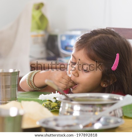 Indian family dining at home. Candid photo of Asian child self feeding rice with hand. India culture.