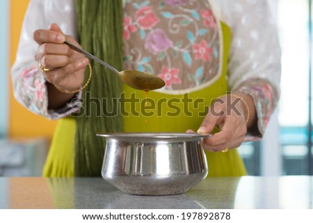Close up ?Indian woman preparing meal, stirring curry sauce, focus on the bowl.