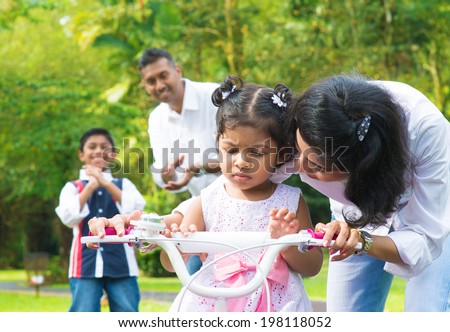 Indian family outdoor activity. Asian mother teaching little girl to ride a bike at the park in the morning.