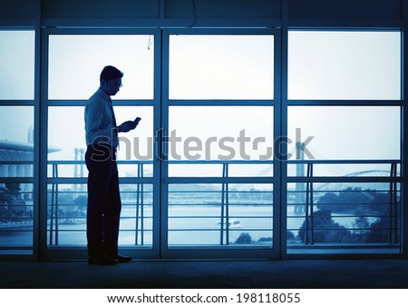 Silhouette of Asian Indian man using mobile phone in modern office building, blue tone.