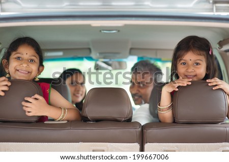 Happy Indian family sitting in car smiling, ready to vacation.  Asian parents and children.