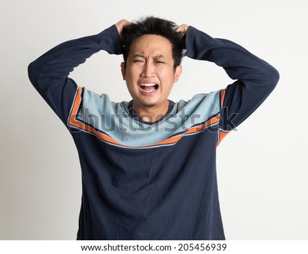 Portrait Of Mad Asian Man Pulling His Hair On Plain Background