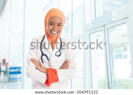 Cheerful young Muslim female doctor portrait, standing inside hospital