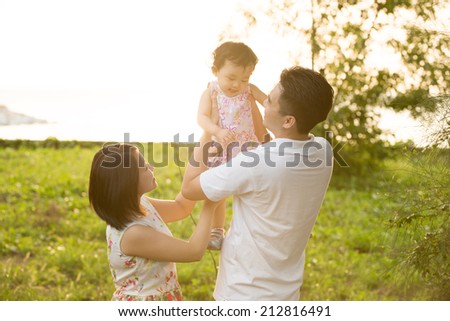 Happy Asian family playing in meadow during summer sunset, outdoors shot.