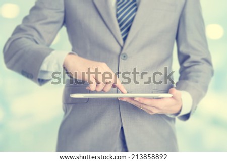 Close-up of male hands touching digital tablet, formal businessman standing with blur background.