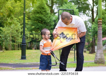 Father teaching son to fly a kite at outdoor garden park. Happy Southeast Asian family living lifestyle.