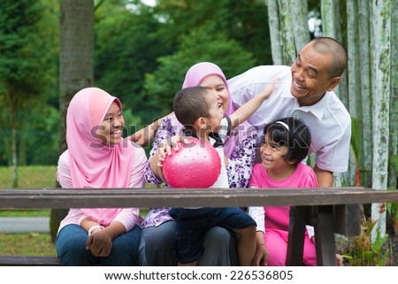 Happy Southeast Asian family sitting at garden bench having fun, outdoor lifestyle at nature green park.
