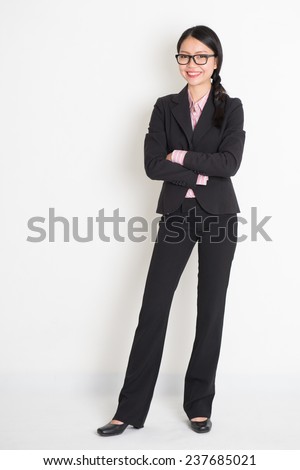 Full body Asian business woman smiling and standing on plain background.