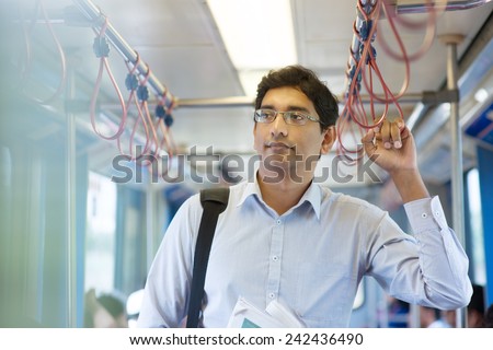 Asian Indian business man taking ride to work, standing inside train.