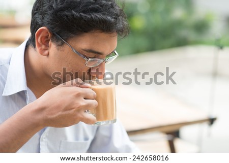 Asian Indian businessman sipping a cup hot milk tea during lunch hour at cafeteria.