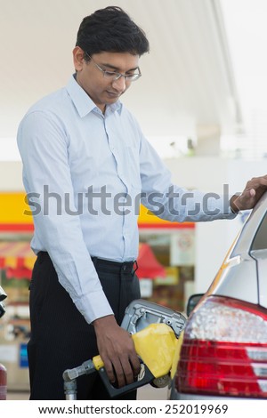 Pumping gas. Asian Indian man pumping gasoline fuel in car at gas station.