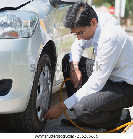 Indian driver checking air pressure and filling air in the tires of his car.