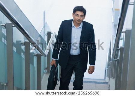 Asian Indian corporate businessman in suit with briefcase ascending steps.