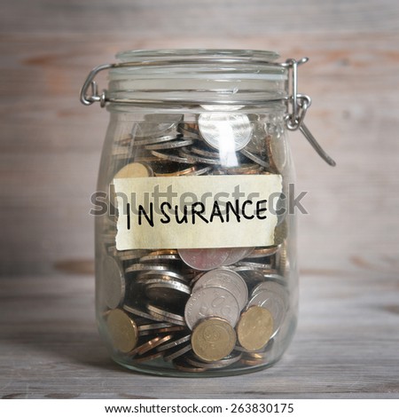 Coins in glass jar with insurance label, financial concept. Vintage wooden background with dramatic light.