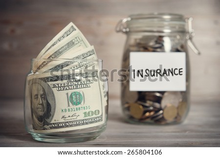 Dollars and coins in glass jar with insurance label, financial concept. Vintage tone wooden background with dramatic light.
