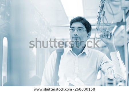 Asian Indian man taking public transport to work, standing inside bus.
