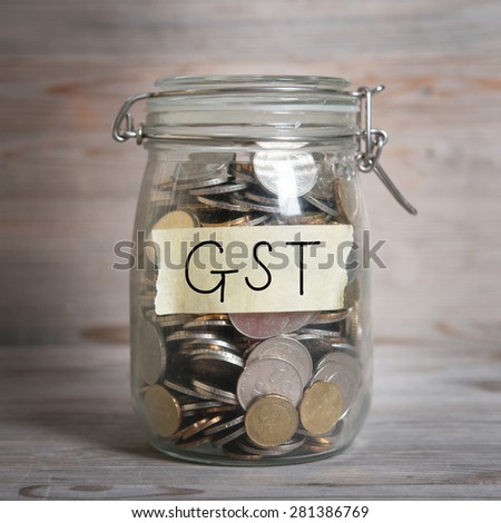 Coins in glass money jar with gst label, financial concept. Vintage wooden background with dramatic light.