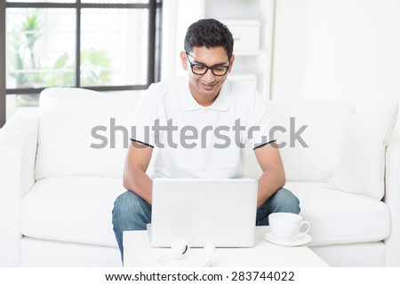 Young Indian guy start his new business with laptop computer from home. Asian man using internet indoor, relaxed and sitting on sofa. Handsome male model working indoors.