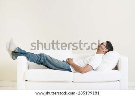 Indian guy daydreaming and rest at home. Asian man relaxed and sleep on sofa indoor. Handsome male model.