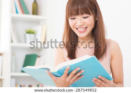 Portrait of happy Asian college girl laughing while reading on book. Young woman at school library.