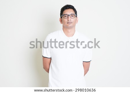 Portrait of bored Indian guy with serious face expression. Asian man standing on plain background with shadow and copy space. Handsome male model.