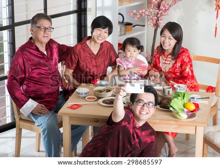 Chinese New Year celebration, reunion dinner. Happy Asian Chinese multi generation family with red cheongsam selfie while dining at home.