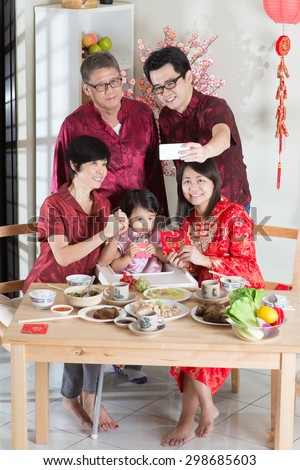 Happy Chinese New Year, taking selfie at reunion dinner. Happy Asian Chinese multi generation family with red cheongsam dining at home.