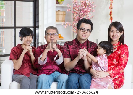 Celebrating Chinese new year. Happy Asian multi generations family in red cheongsam reunion and greeting at home.