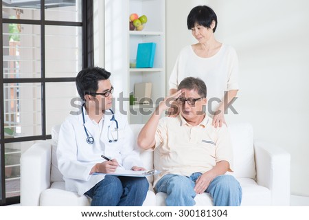 Doctor and patient. Asian old man headache, consult family doctor, sitting on sofa. Senior retiree indoors living lifestyle.
