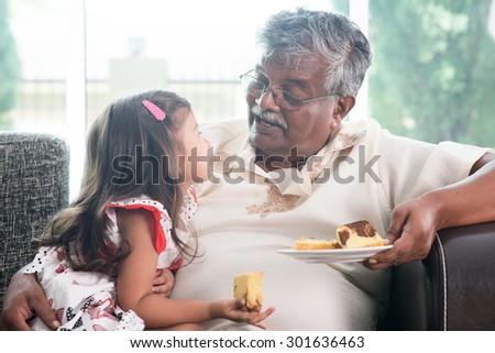 Portrait of Indian family at home. Grandparent and grandchild eating butter cake. Asian people living lifestyle. Grandfather and granddaughter.