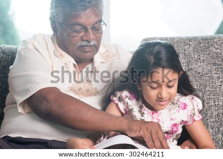 Grandparent and grandchild reading story book together. Happy Indian family at home. Asian grandfather and granddaughter indoor lifestyle.