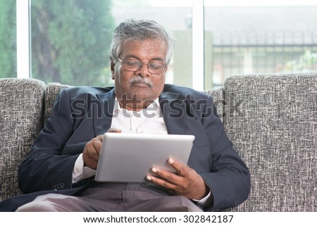 Modern technology. Old Indian man using touch screen tablet computer at home. Asian senior people living lifestyle indoors.