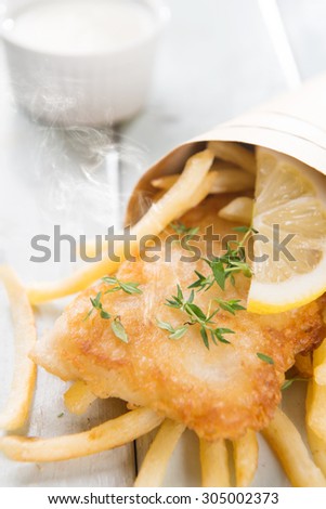 Fish and chips. Fried fish fillet with french fries wrapped by paper cone, on wooden background. Fresh cooked with hot steams.