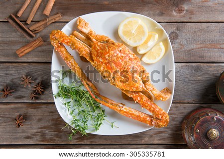 Top view cooked delicious hot and spicy sauce blue crab on white plate with herb ingredients, at wood background. Fresh cook with hot smoke steams.