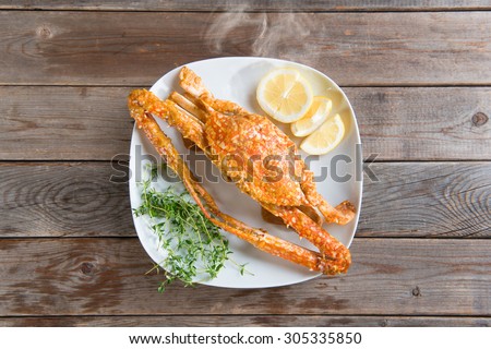 Top view cooked delicious hot and spicy sauce blue crab on white plate, at wood background. Fresh cook with hot smoke steams.