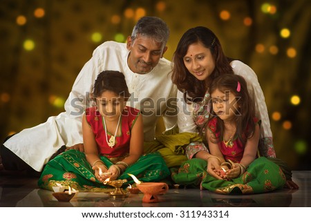 Indian family in traditional sari lighting oil lamp and celebrating Diwali, fesitval of lights inside a temple. Little girl hands holding oil lamp indoors.