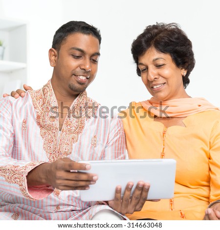 Portrait of Indian family using social media at home. Mature 50s Indian woman and son looking at tablet computer.