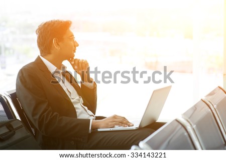 Business man using laptop while waiting his flight at airport, beautiful golden sunset background.