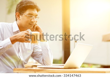 Man using laptop computer while drinking a cup hot milk tea, outdoor cafe, beautiful sunlight during sunset.